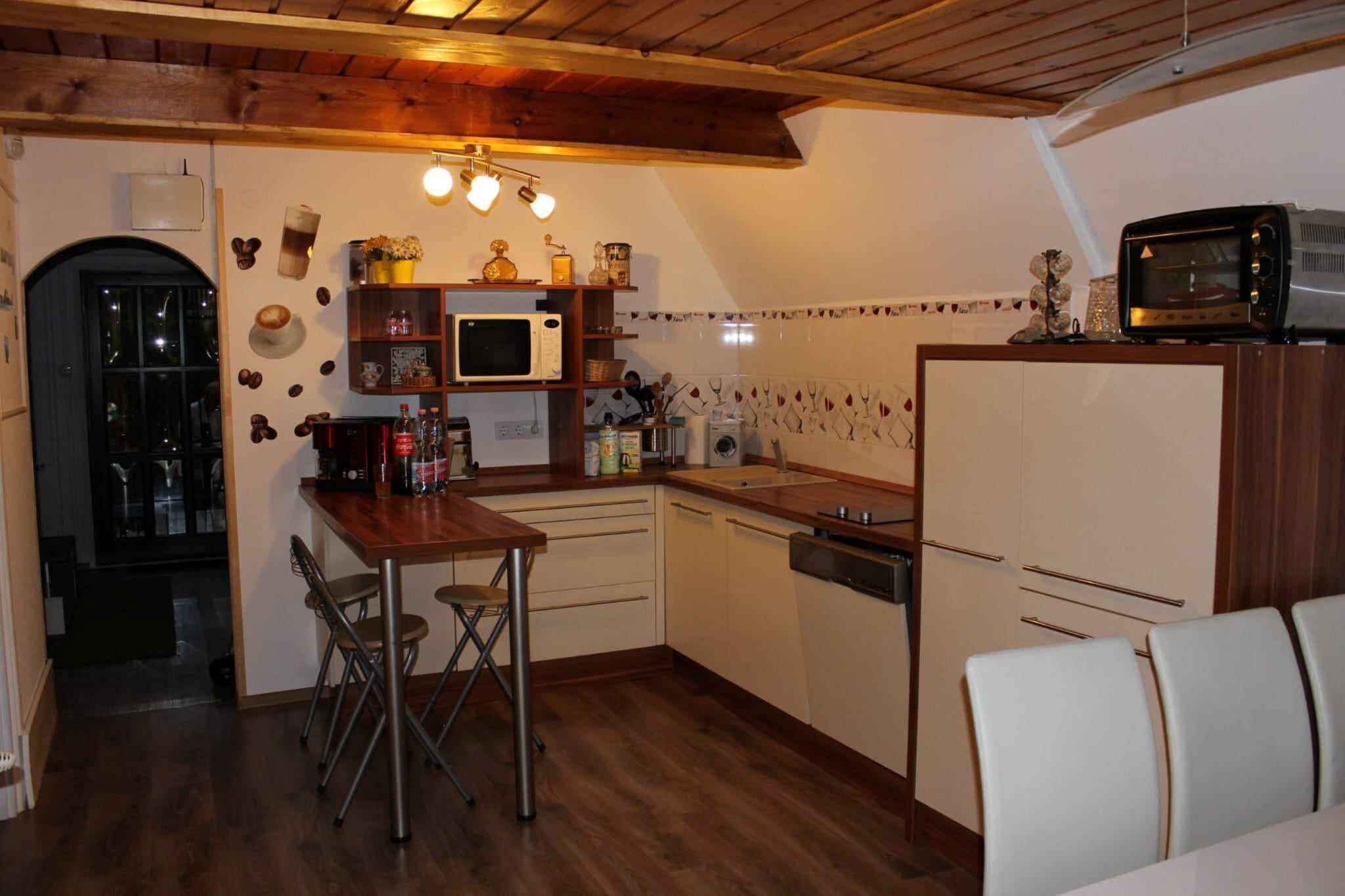 Cocina compacta con armarios de madera, microondas, tostadora y comedor con sillas.