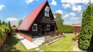 A two-story wooden house with a red roof, a small porch, and a fenced yard.