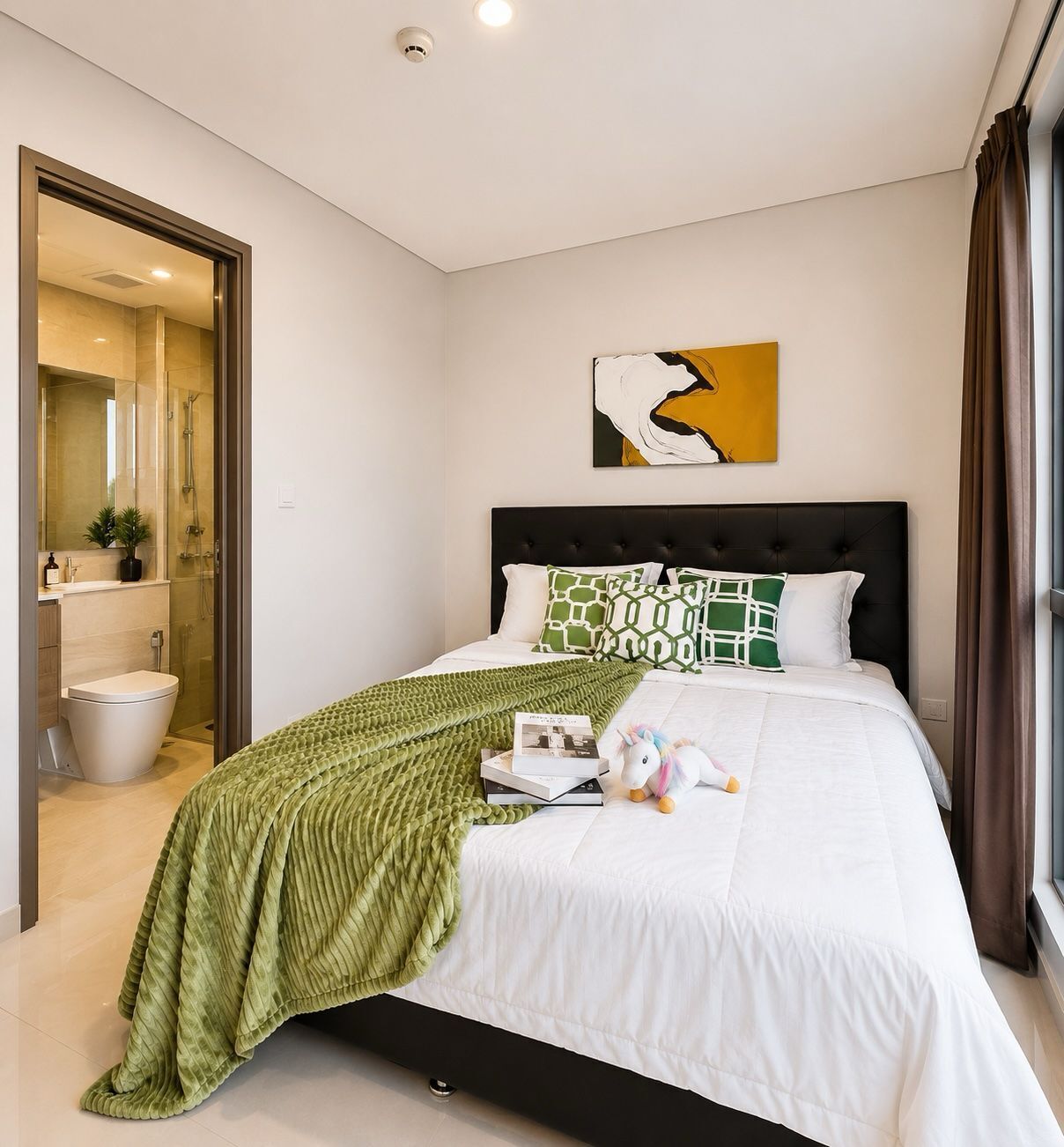 Een slaapkamer met een bed, een groene deken, een wit kussen, een lijst met abstract schilderij, en een badkamer met toilet en douche.