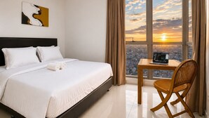 Una camera d'albergo con un letto, un portatile su un tavolo, una sedia e vista sulla città.