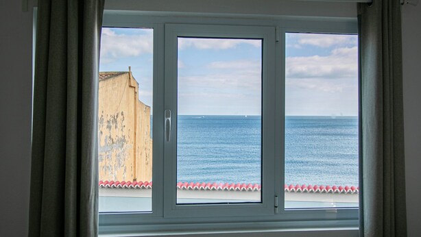 A window with a view of the sea and a building with peeling paint.
