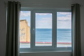 A window with a view of the sea and a building with peeling paint.