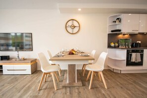 A modern kitchen with a dining table set for four, a clock on the wall, and built-in cabinetry. - Baltic Village im Ostseebad Damp (Damp)