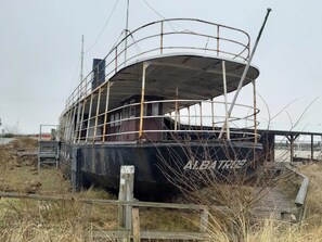 An abandoned ship with a curved deck and a cabin structure, surrounded by overgrown vegetation. - Baltic Village im Ostseebad Damp (Damp)