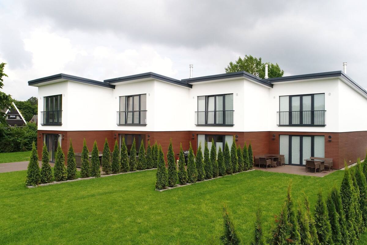 A modern two-story residential building with a flat roof, large windows, and a well-maintained lawn with neatly trimmed hedges.