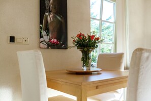 A dining area with a wooden table, white chairs, a vase with flowers, and a Buddha painting on the wall. - Apartment in Oostkapelle Near the Beach (Oostkapelle)