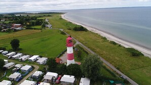 Uma área costeira com um farol vermelho e branco imponente, uma praia e um parque de caravanos.