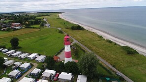 A coastal area with a prominent red and white lighthouse, a beach, and a caravan park. - Baltic Village in Damp am Ostseestrand (Damp)