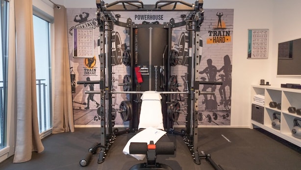 A gym with a squat rack, weight plates, and motivational posters on the wall. - Geraumiges Ferienhaus in Damp in Strandnahe (Damp)