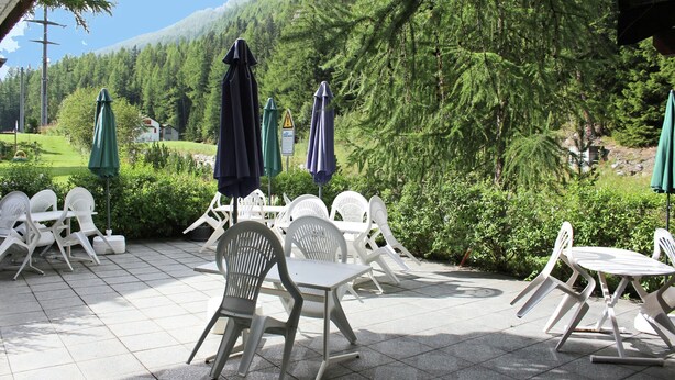 An outdoor patio with white plastic chairs and tables, green umbrellas, and a view of a forested hillside. - Holiday Home in Nysted by Baltic Sea (Saas-Balen)