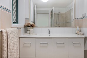 Ein Badezimmer mit einem weißen Waschbecken, einem Spiegel und einer Dusche.