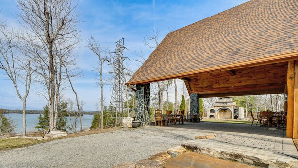 A lodge with a stone facade, outdoor seating, and a view of a lake. - Steps to Private Beach! Family Home on Lake James (Nebo)