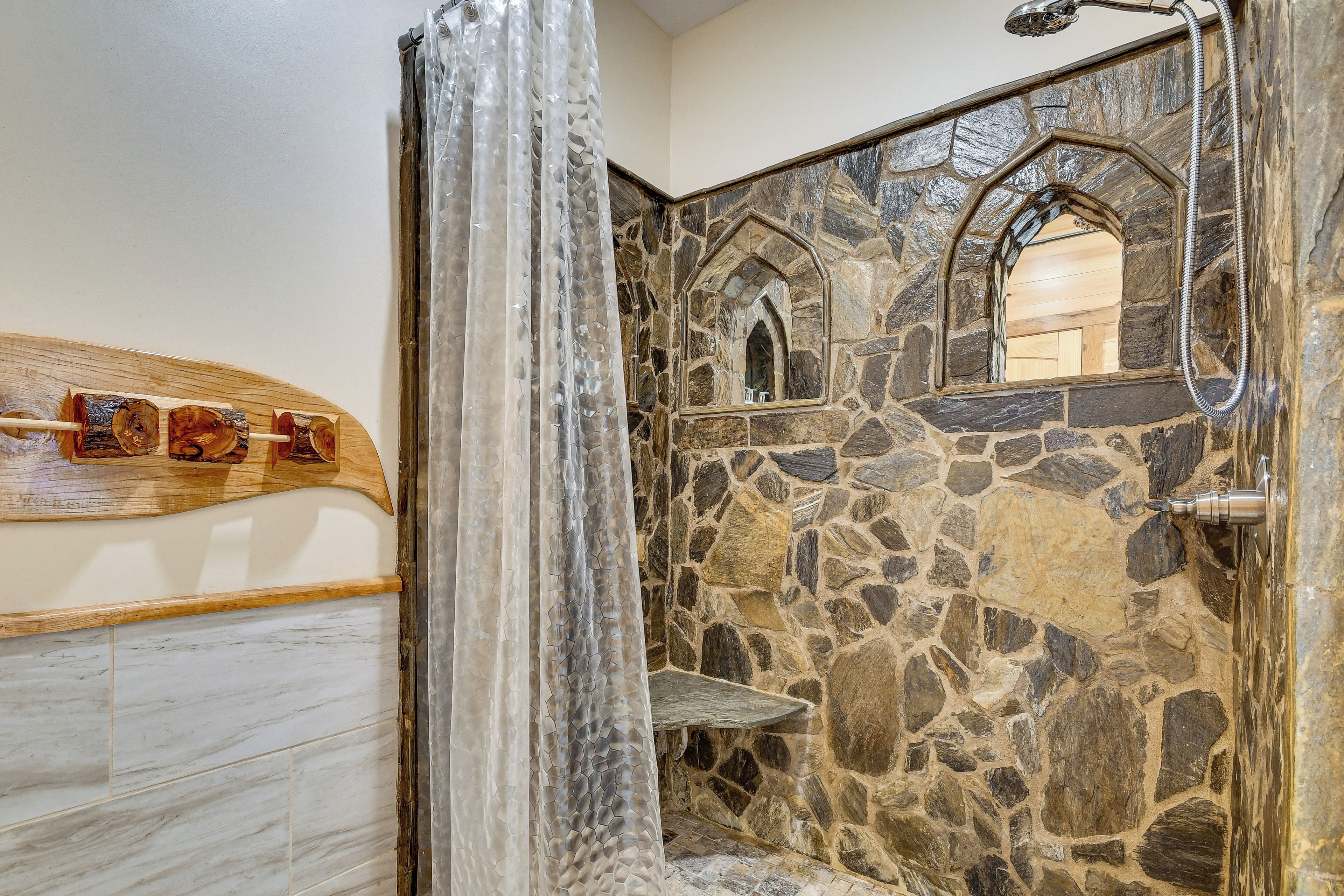 Une douche aux murs en pierre, avec une étagère en bois et une pomme de douche suspendue.