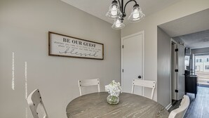 A dining area with a round table, white chairs, a vase with flowers, and a wall sign. - 5 Mi to Cave Tour! Couples Adventure Hub (Bowling Green)