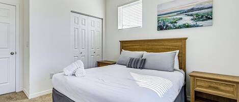 A bedroom with a large bed, a wooden headboard, a nightstand, a painting on the wall, and a closet.