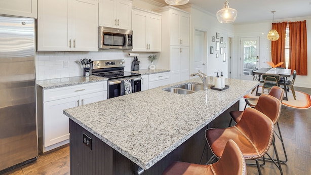 Una cocina moderna con armarios blancos, electrodomésticos de acero inoxidable, encimeras de granito y una isla central con taburetes de bar.