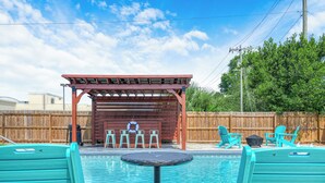 A backyard with a swimming pool, a covered seating area, and a wooden fence.