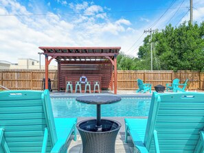 Un cortile con piscina, zona relax coperta e recinzione in legno.