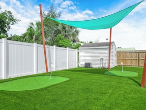 Un jardin avec une clôture blanche, un abri de jardin et une zone recouverte de gazon synthétique vert.