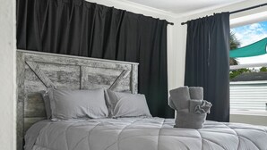 A bed with a grey quilt, black curtains, and a grey headboard.