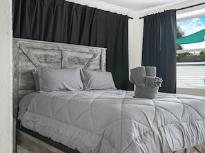Un letto con una coperta grigia, tende nere e una testiera grigia.