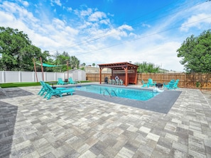 Un jardin avec une piscine, des meubles de patio et un espace salon abrité.