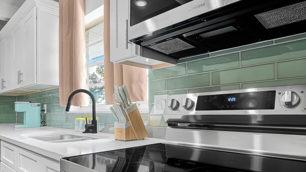 A modern kitchen with stainless steel appliances, including an oven and a stovetop, and a window with curtains.