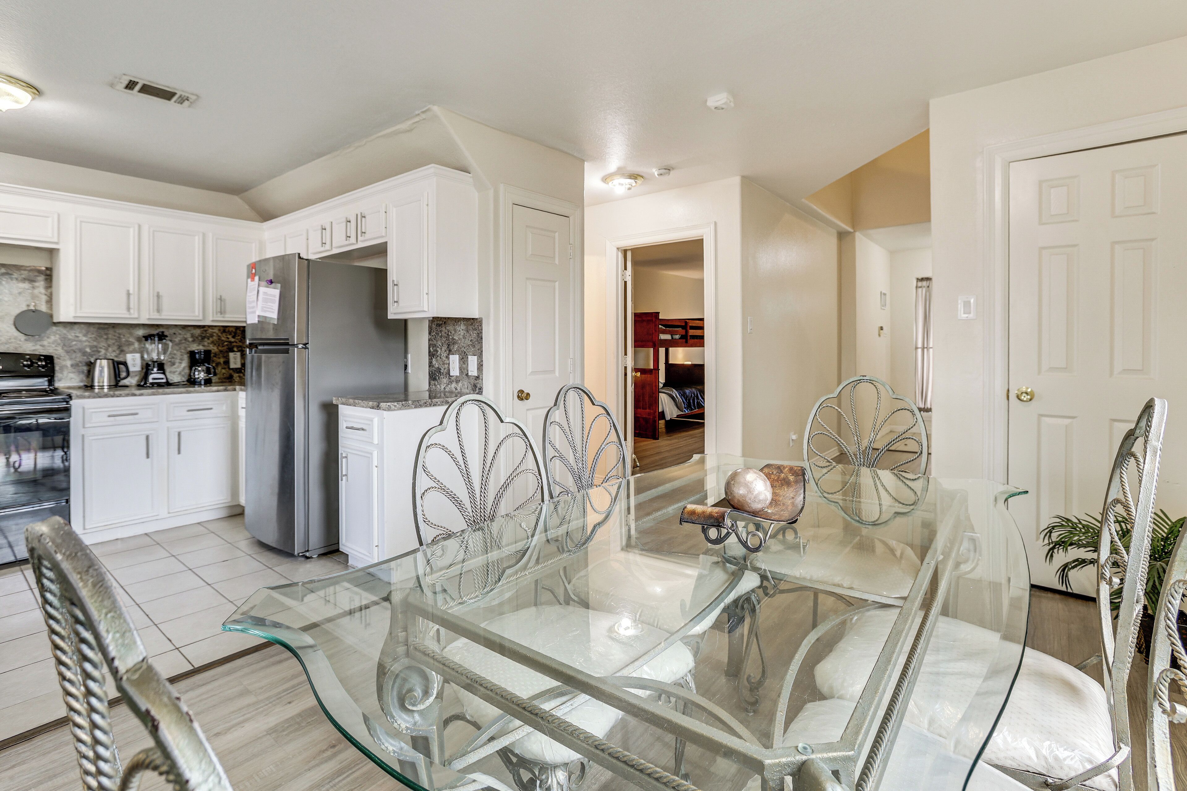 A modern kitchen with white cabinets, stainless steel appliances, and a glass dining table with metal chairs.
