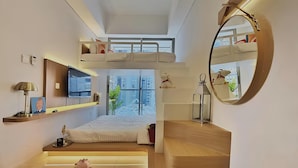 Ein gemütliches, modernes Schlafzimmer mit Etagenbett, Nachttisch mit Lampe, Spiegel und Blick auf die Stadt durch ein großes Fenster.