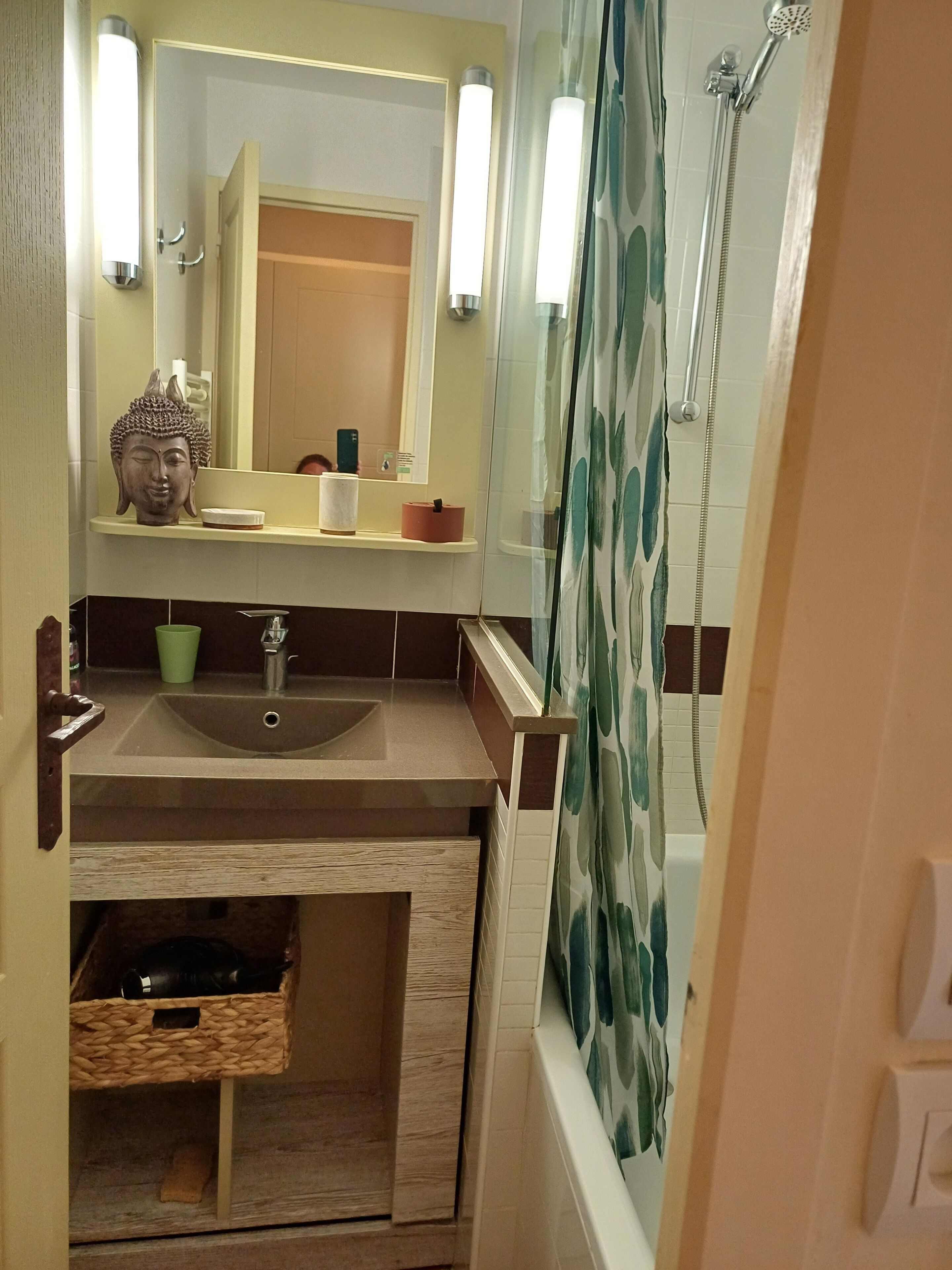 Une salle de bain équipée d’un lavabo, d’un miroir, d’un rideau de douche et d’une tête de Bouddha décorative.