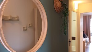 Un pasillo con un espejo redondo en la pared, una cesta tejida y una planta en maceta.