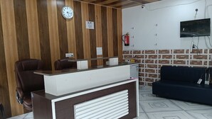 Un'area reception con parete in legno, un orologio, un estintore, una televisione e un divano.