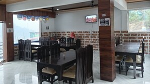Un ristorante con travi a vista in legno, pareti in piastrelle e un'ampia finestra. Tavoli e sedie disposti per consumare pasti.