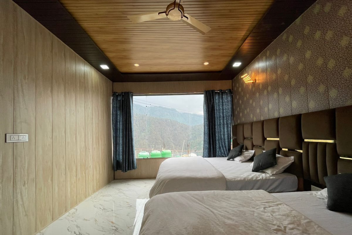 Habitación de hotel con dos camas, techo de madera, ventana con cortinas y vistas a montañas.