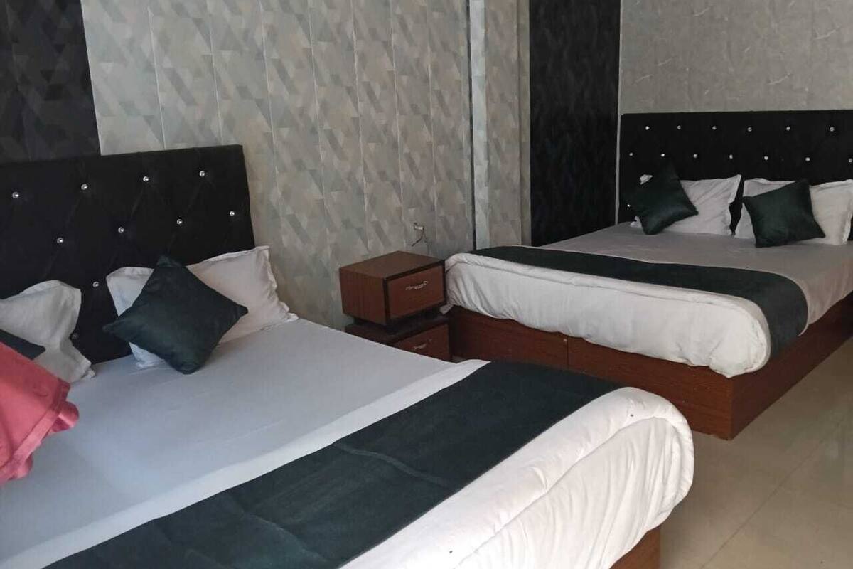 Dos camas individuales con cabeceras, ropa de cama blanca y almohadones verde oscuro.
