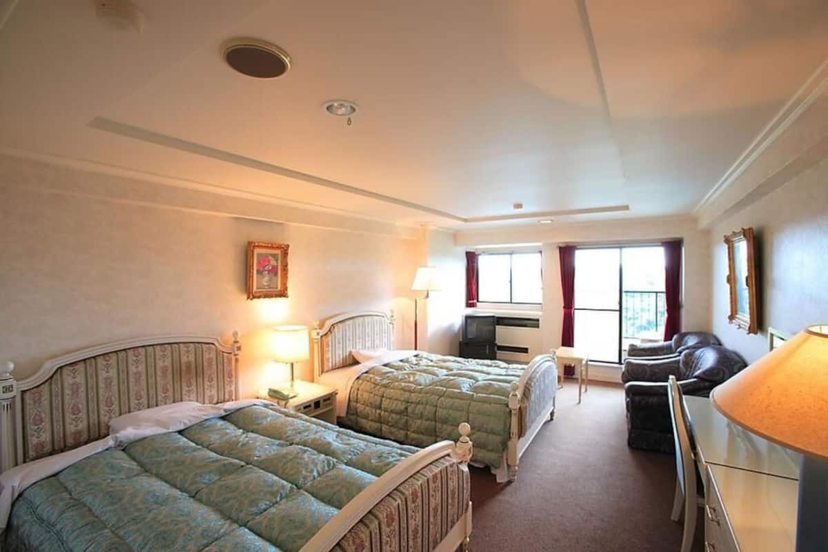 Une chambre d’hôtel avec deux lits simples, un bureau, une chaise et une fenêtre avec des rideaux.
