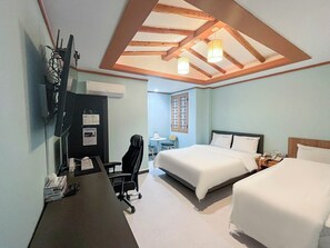 Et hotelværelse med en seng, et skrivebord med stol, et fjernsyn og et loft med træbjælker og hængende lamper.