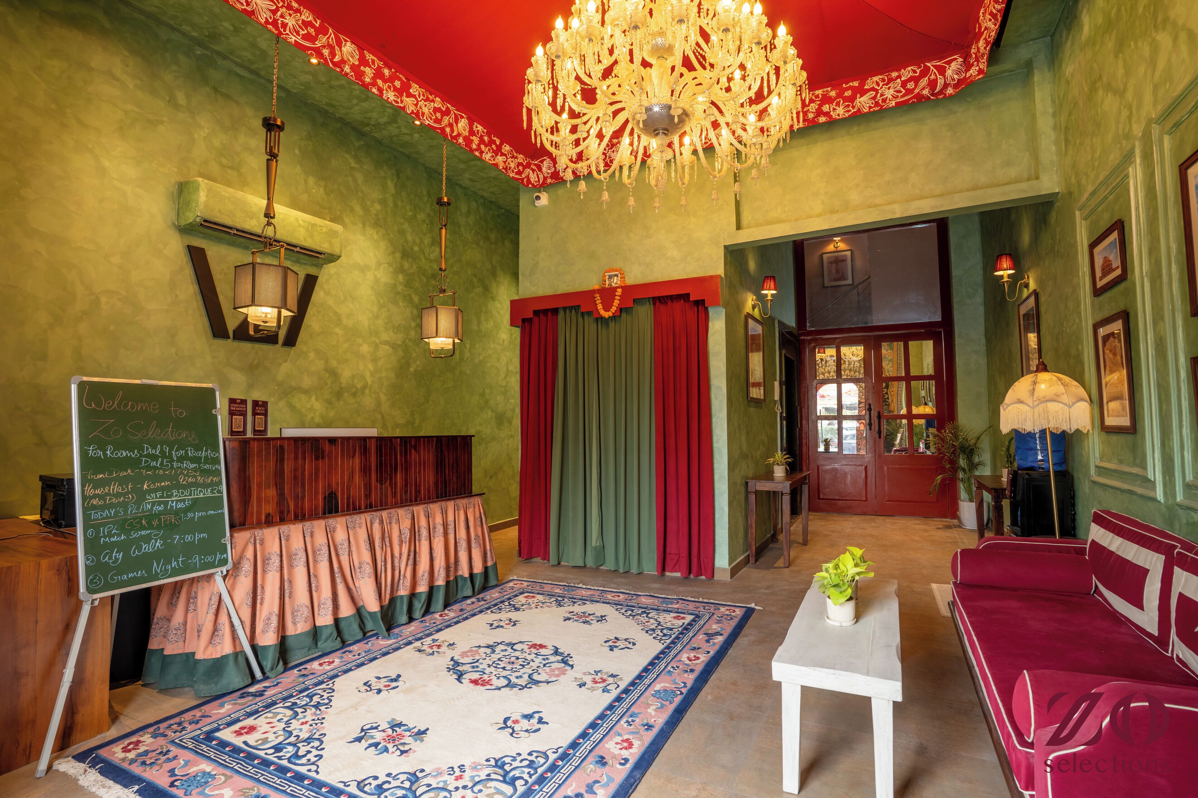 Una habitación con candelabro, techo rojo, pared verde, sofá rojo, mesa blanca y alfombra estampada.