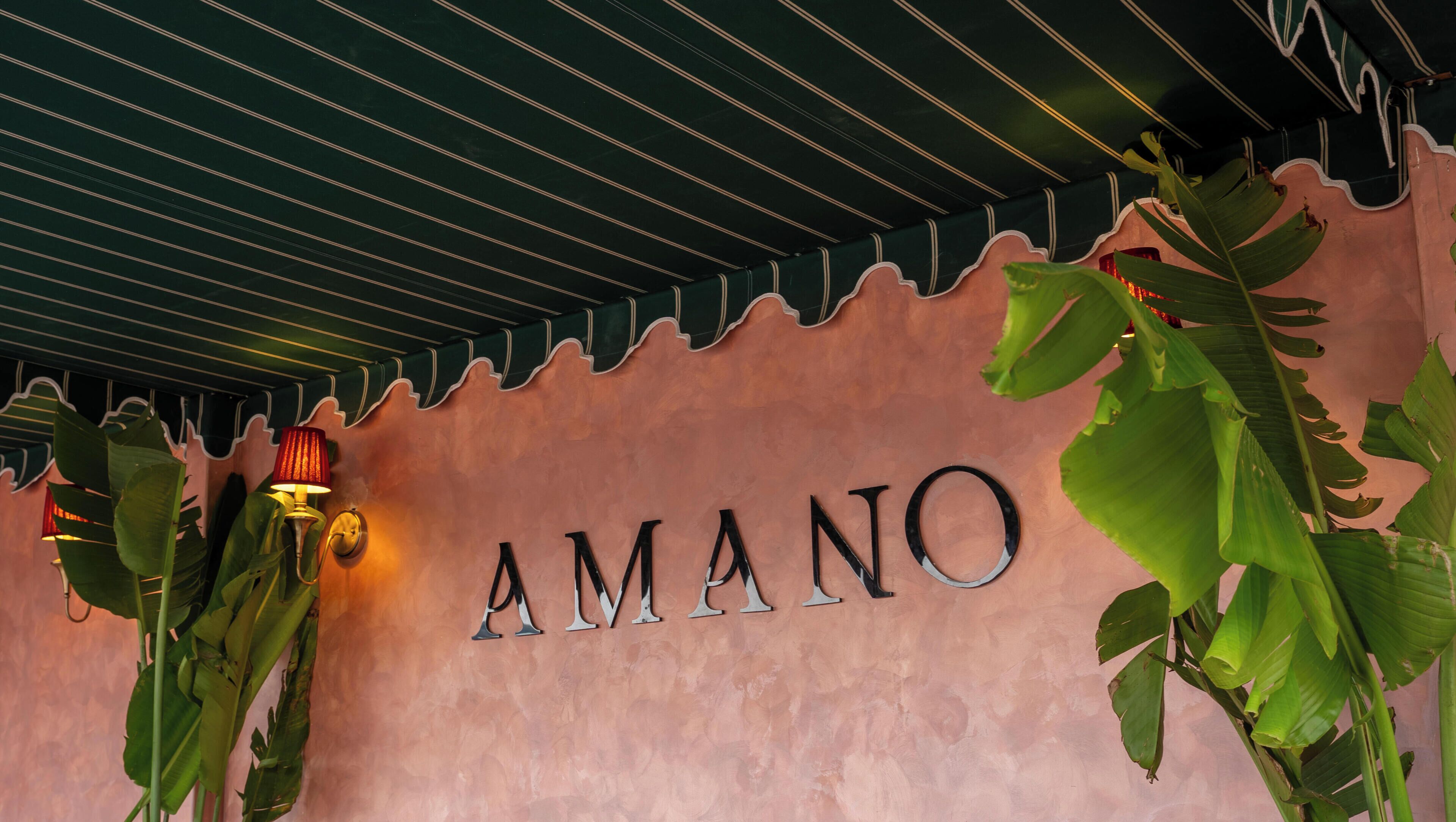 A wall with the name 'AMANO' in large letters, a decorative light fixture, and green foliage.