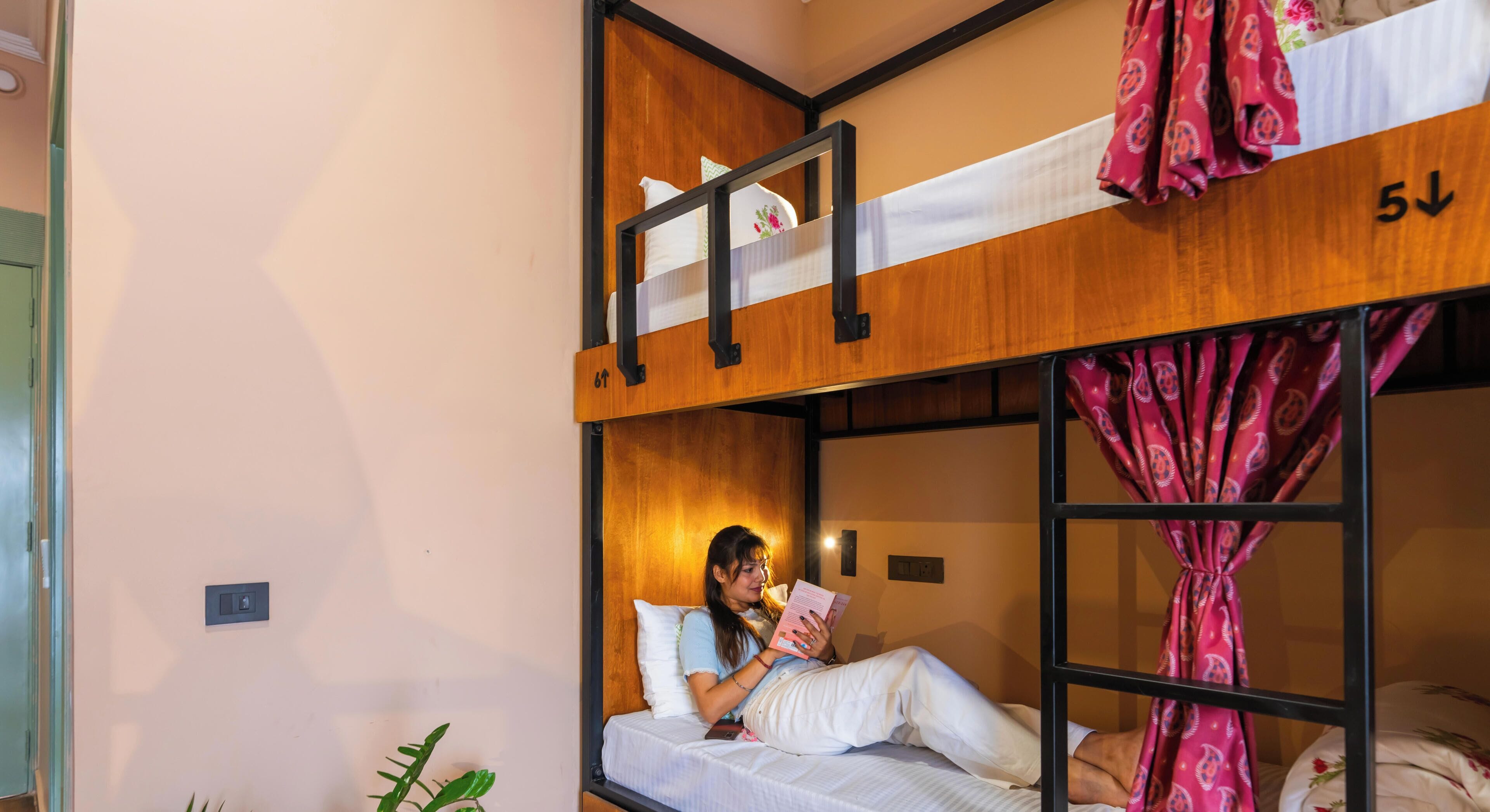 Habitación con literas, una persona leyendo un libro, una puerta y un interruptor de luz en la pared.
