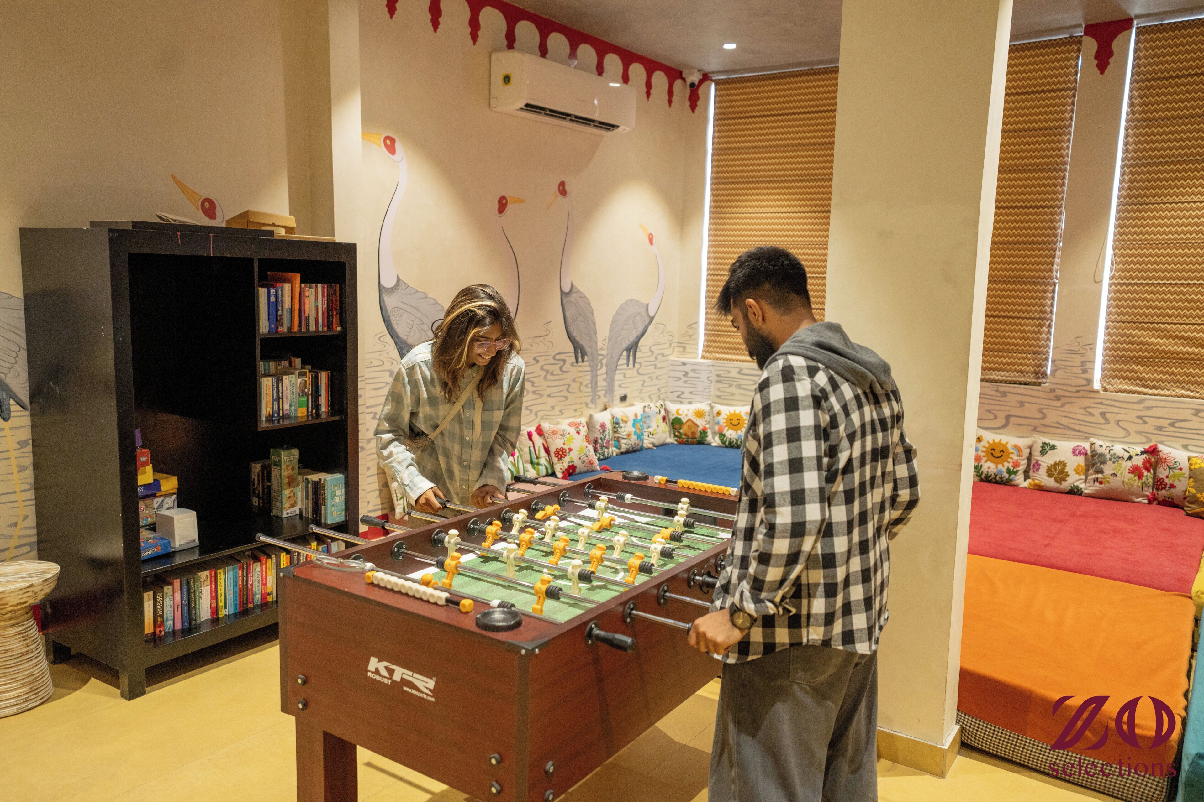 A room with a foosball table, a bookshelf, and a bed with colorful bedding.