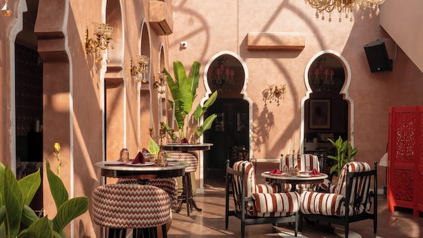Un patio con mesas redondas, sillas con cojines a rayas y un biombo decorativo rojo.