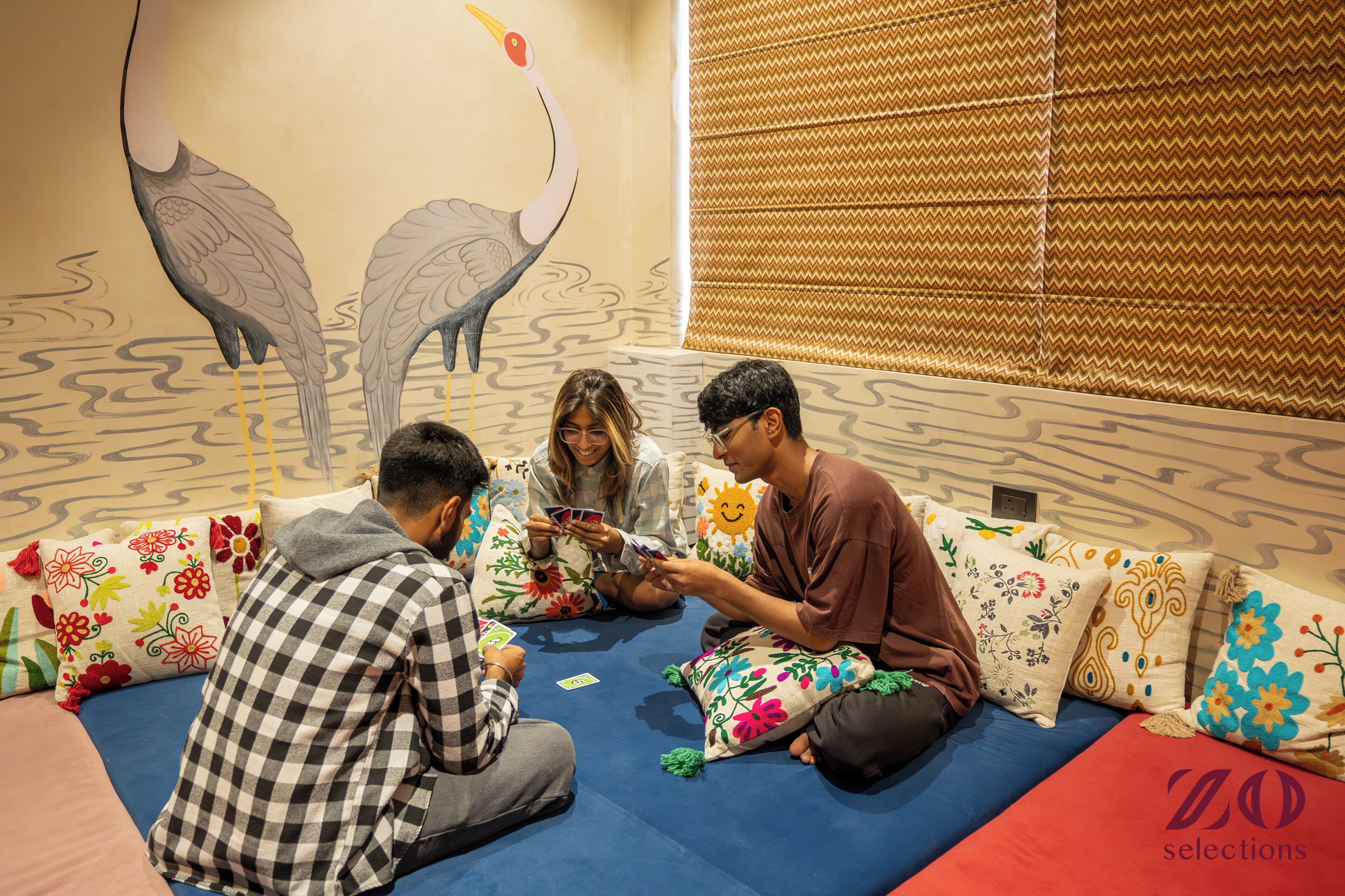 Un grupo de personas sentadas en un sofá azul con almohadones de colores, en una habitación con paredes con diseño y un mural grande.