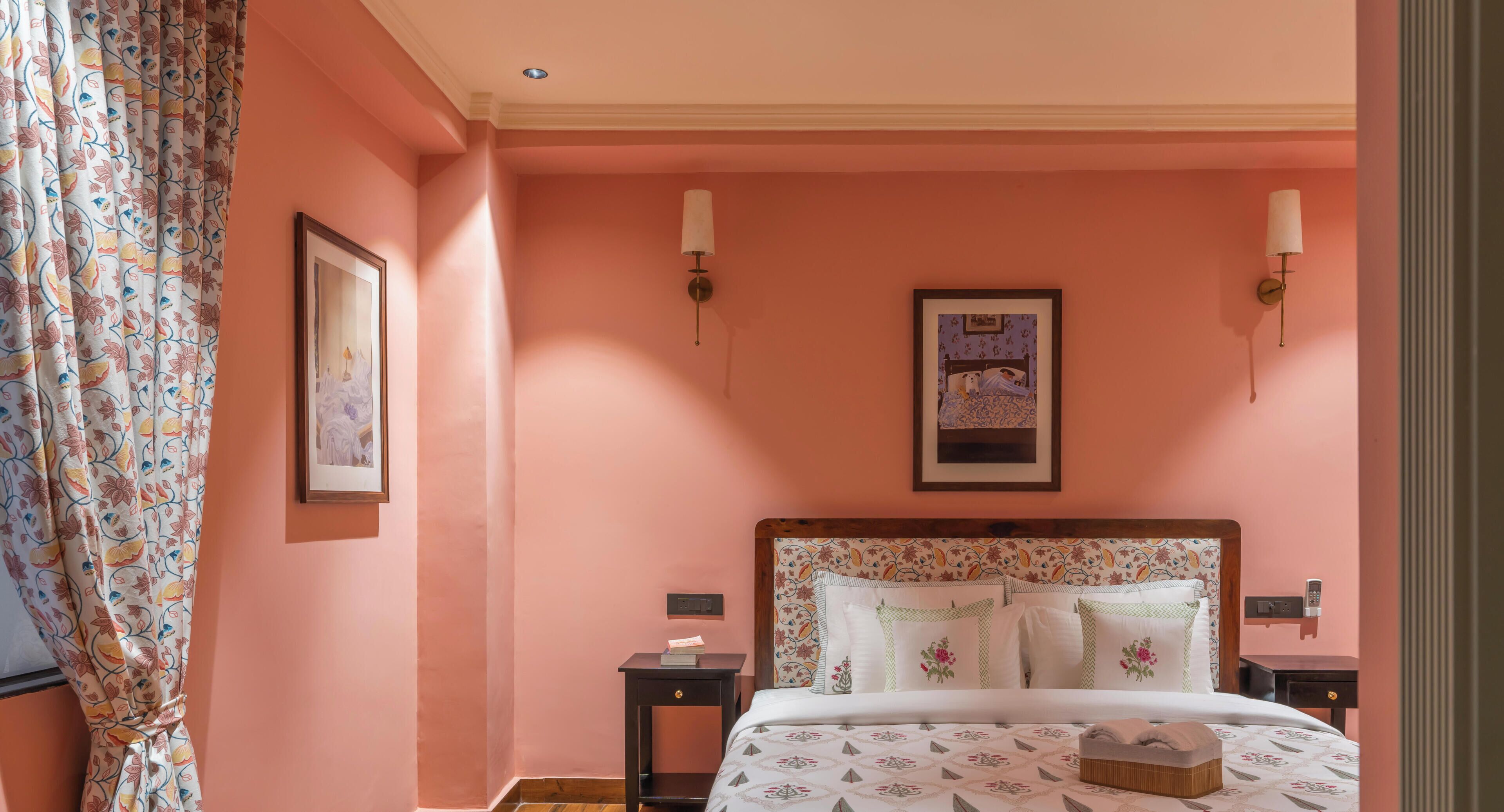 A bedroom with a pink wall, a bed with floral bedding, two bedside tables, and a framed picture above the bed.