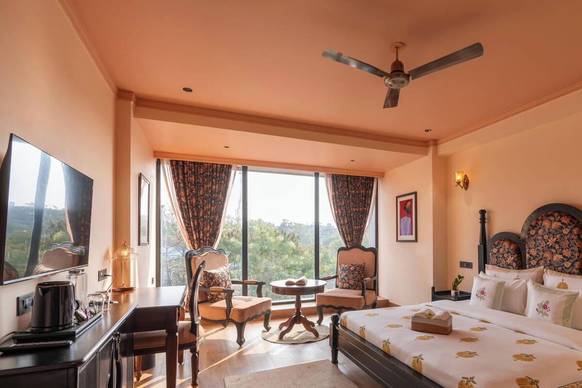 Habitación de hotel con cama, escritorio, silla, ventilador de techo y ventana con cortinas.