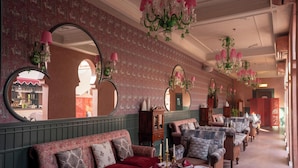 Una habitación con un sofá largo, varios espejos y candelabros colgantes.