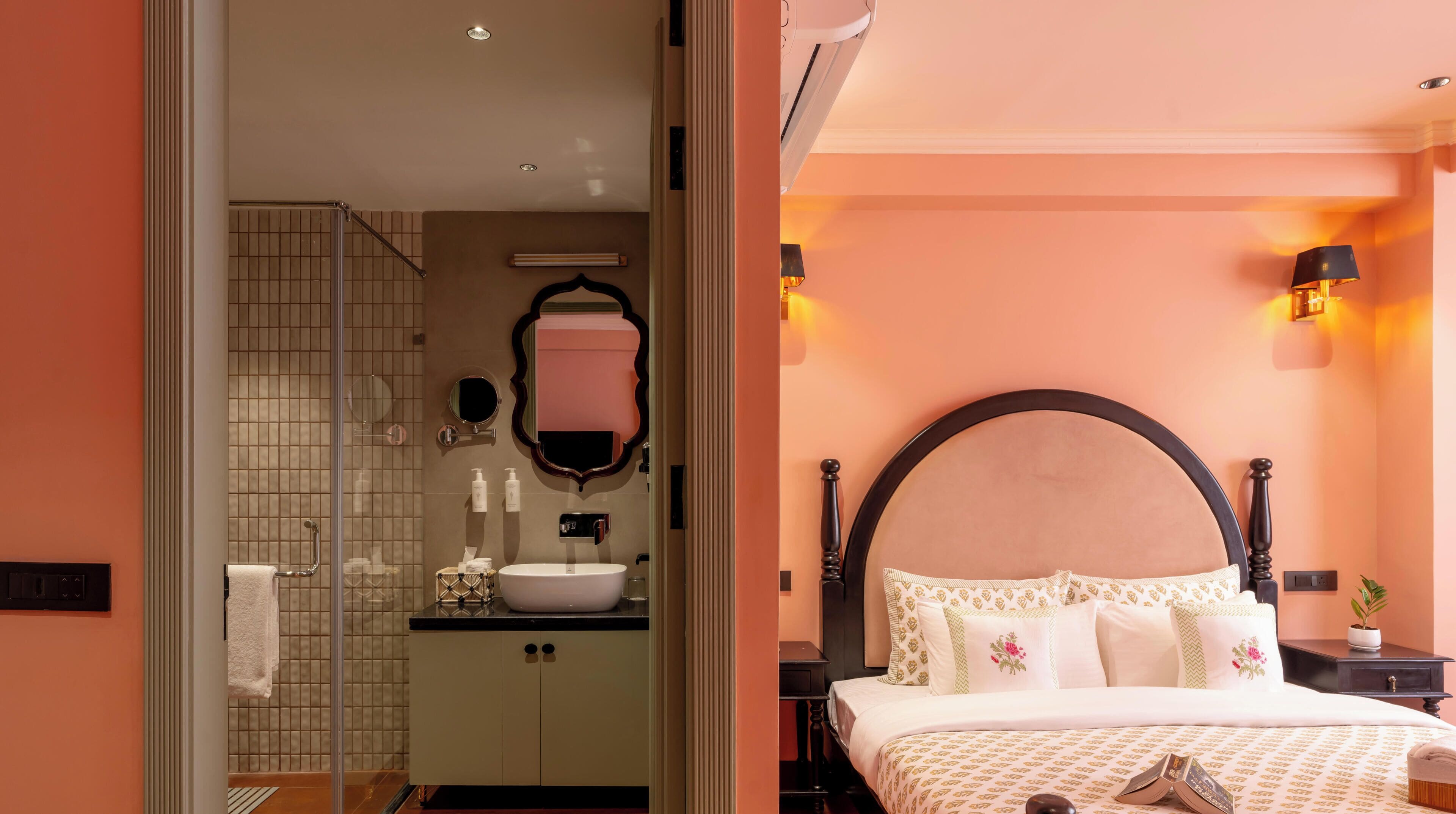 A bathroom with a glass shower, a sink, and a mirror. The room has a warm color scheme and includes a bed with a headboard and pillows.