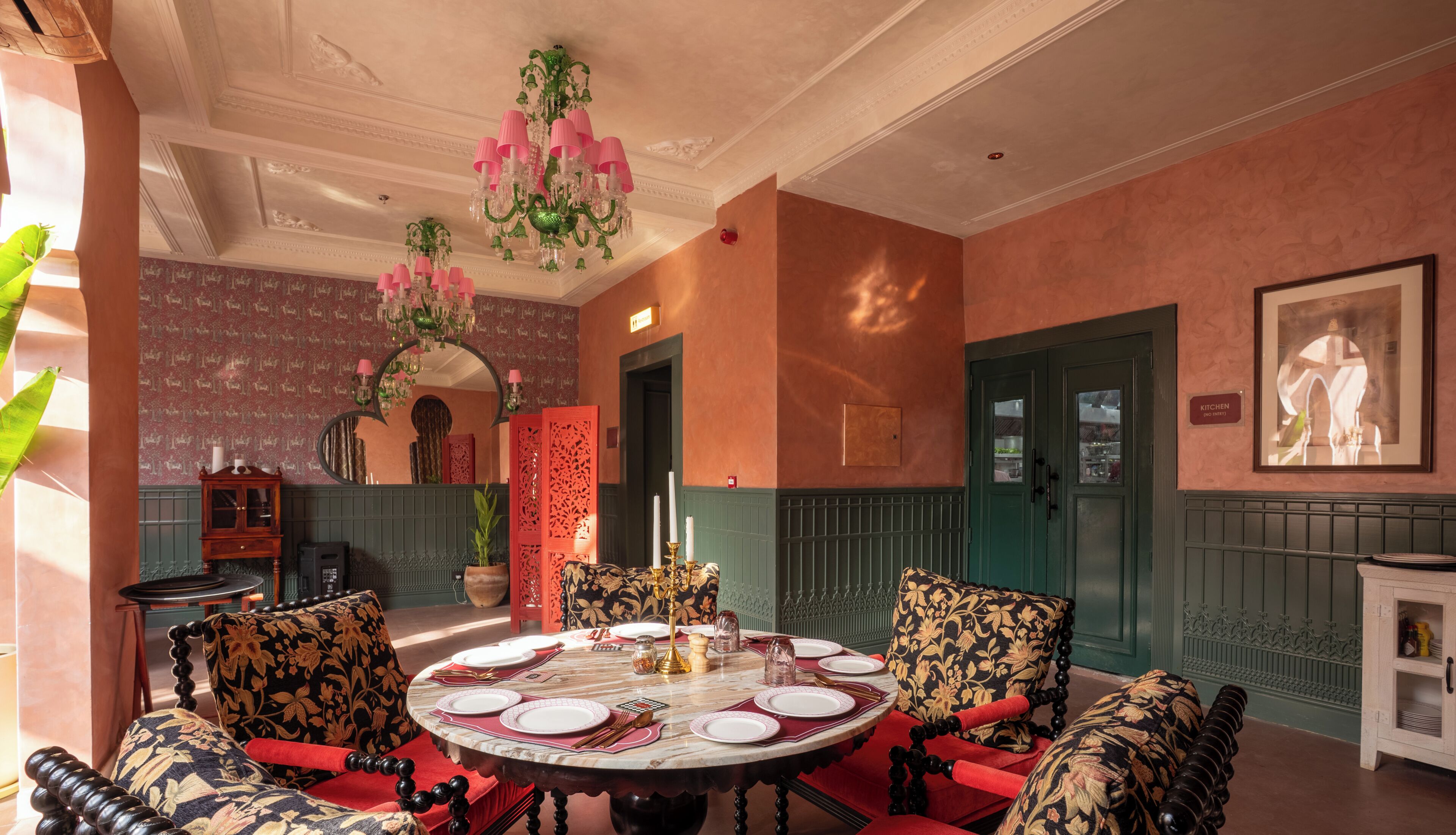 A dining area with a round table set for four, a chandelier, and a mirror above the table.