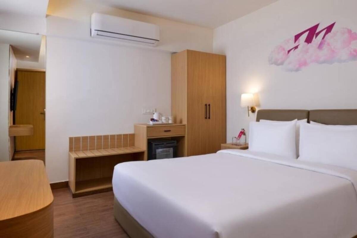 Quarto de hotel com cama grande, escrivaninha, guarda-roupa e ar condicionado fixado na parede.