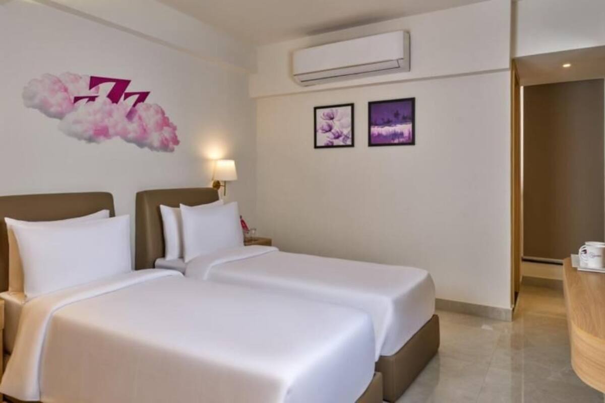 Quarto de hotel com duas camas, uma mesa de cabeceira com abajur, telefone e ar condicionado fixado na parede.